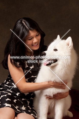 woman cuddling young Samoyed, looking at each other