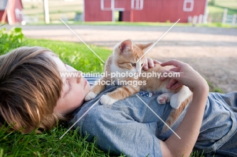 Young boy laying down holding a kitten at a farm.