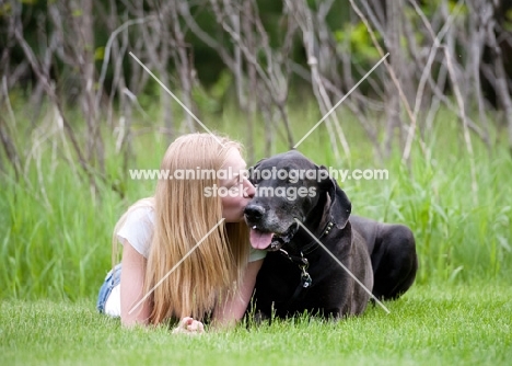 Woman lying with Great Dane, kissing her on the muzzle.