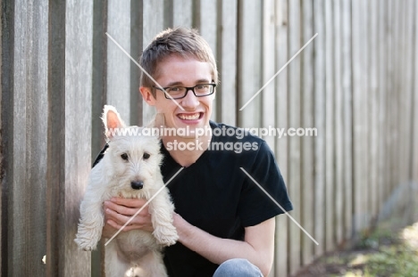 wheaten Scottish Terrier puppy being held by male owner outdoors.