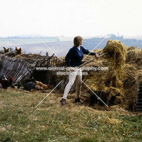 woman with pitchfork at dung heap with chickens in background