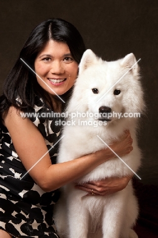 woman cuddling young Samoyed, looking at camera