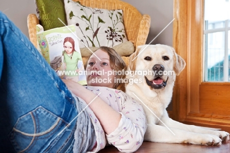 girl reading a book while leaning against a Labrador