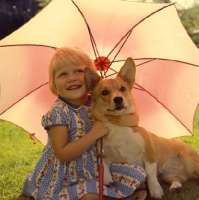 Picture of girl and corgi under parasol looking forward and smiling