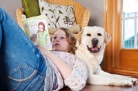 Picture of girl reading a book while leaning against a Labrador