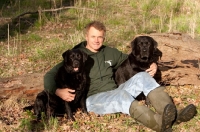 Picture of man sitting in field with two black labradors
