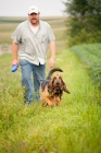 Picture of man with bloodhound walking in grassy field with soybean field to the side