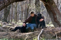 Picture of man with two black labradors sitting in woods