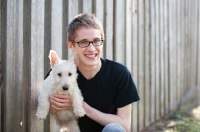 Picture of wheaten Scottish Terrier puppy being held by male owner outdoors.