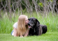 Picture of Woman lying with Great Dane, kissing her on the muzzle.